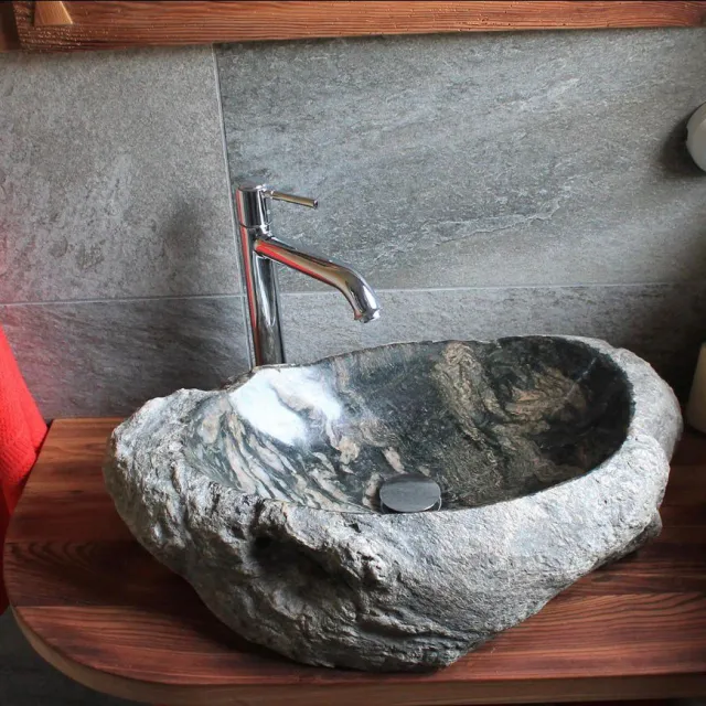 Naturstein-Waschbecken mit Chromarmatur vor Steinfliesen